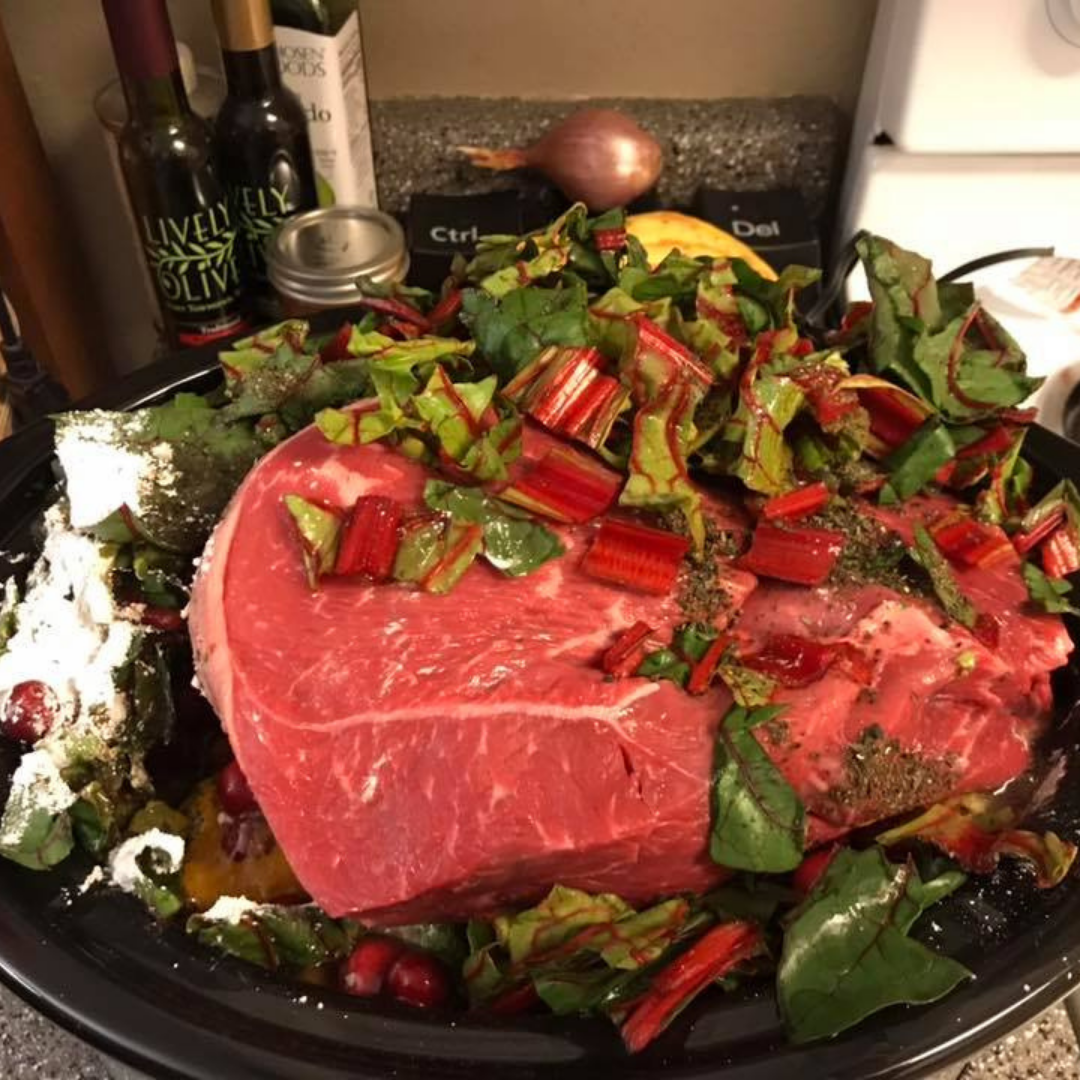 The image shows a black crockpot with a colorful mix of ingredients: diced yellow squash or pumpkin cubes, bright green peas, dark red kidney beans, brown rice with shredded meat (likely ham or corned beef), and chopped carrots. The dish looks vibrant and appetizing, and the clean, shiny crockpot indicates the meal is still in the early stages of cooking.